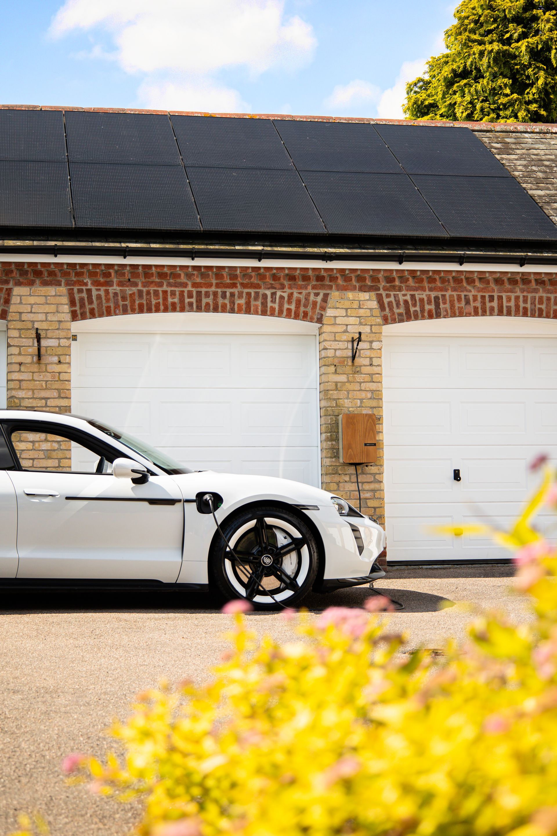 A home EV charger beside a solar-equipped garage on a private driveway